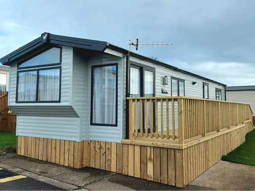 A prefabricated building with grey walls, a black roof and a wooden patio.